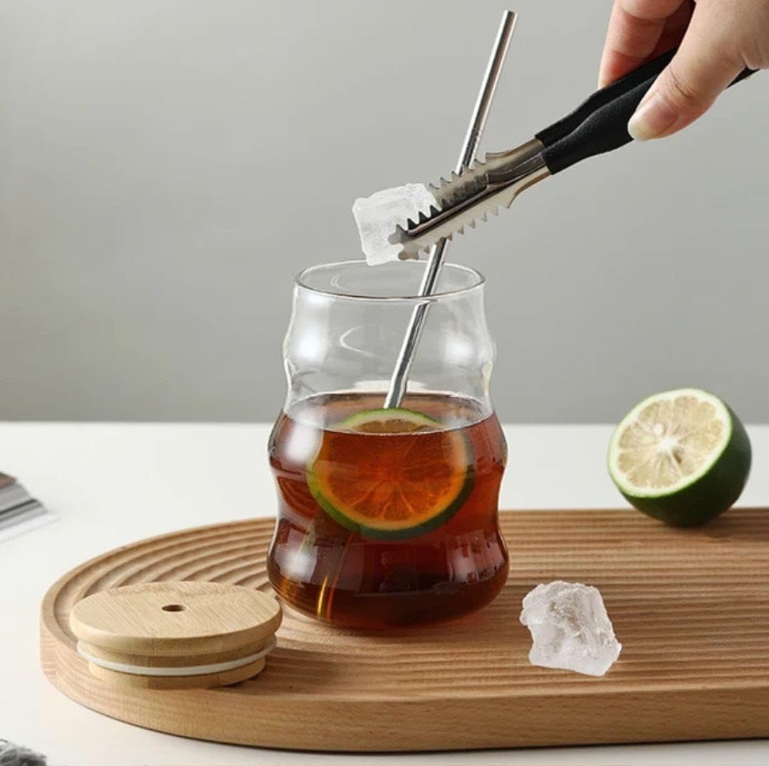 Glass tumbler with straw filled with iced tea with lime and lemon slices on a wooden tray, with a hand using tongs to add ice.